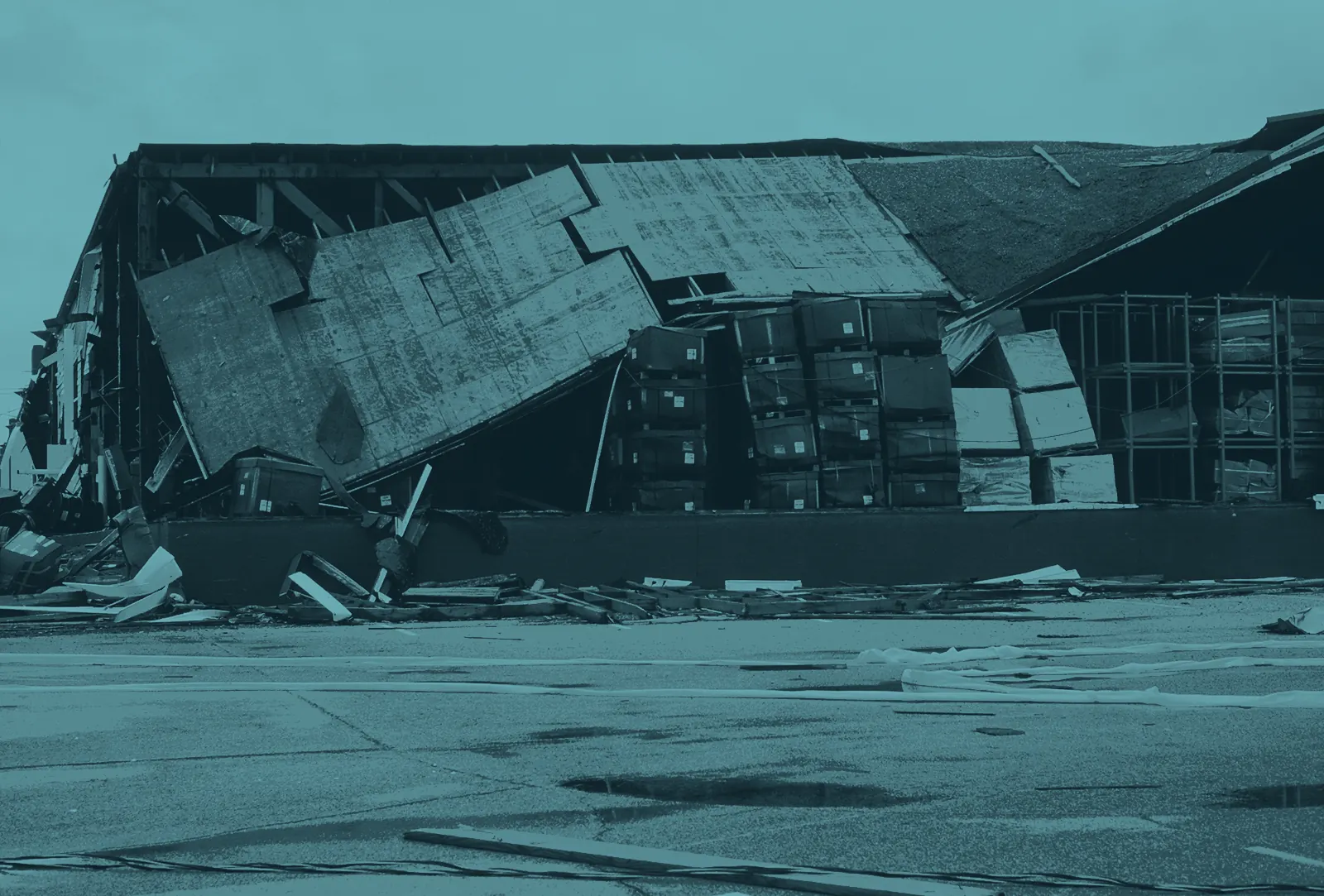 A warehouse whose roof deck has collapsed onto pallets of boxed stock and orange racking