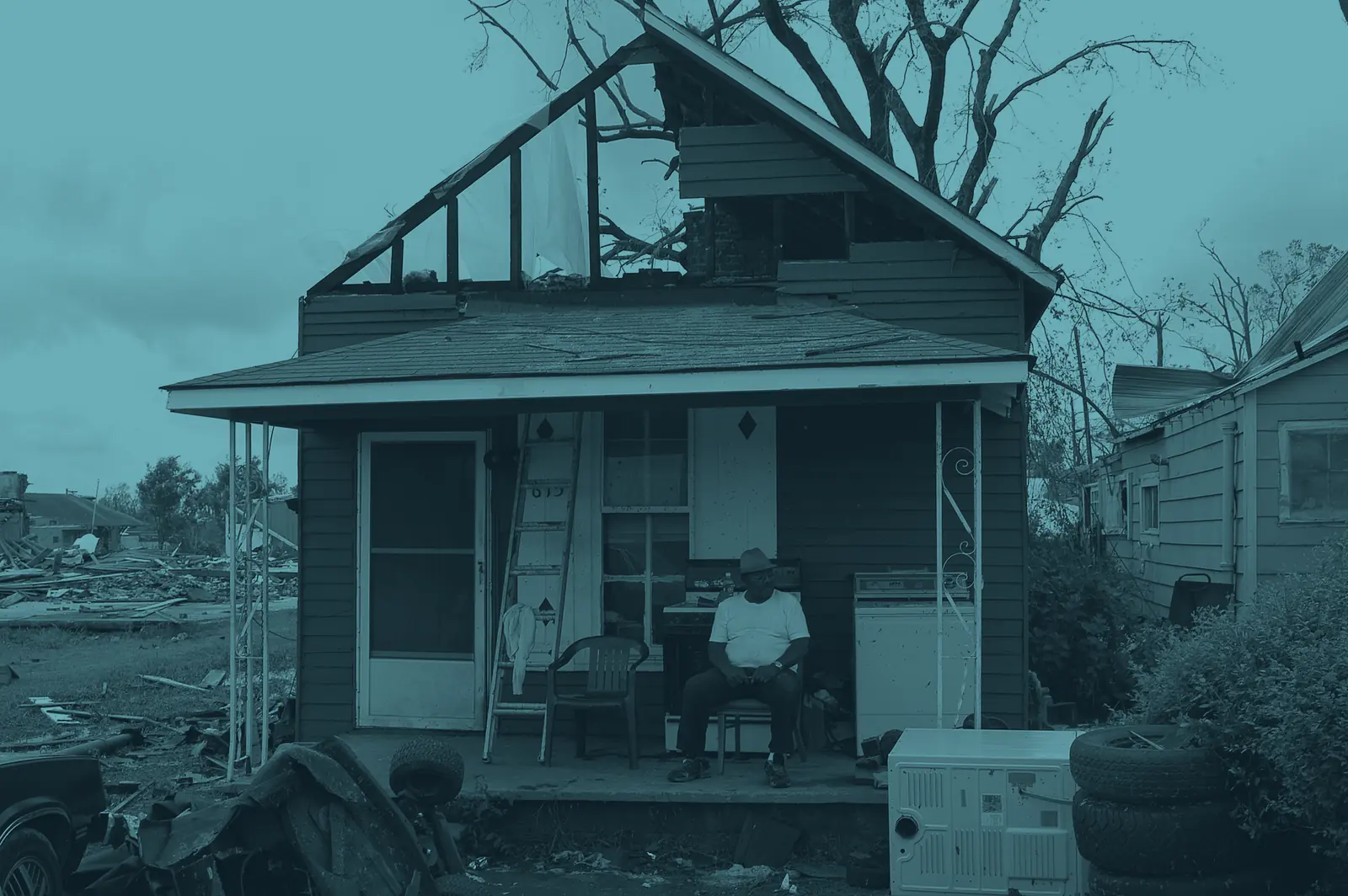 A homeowner sitting on the porch of a house whose roof has been torn away
