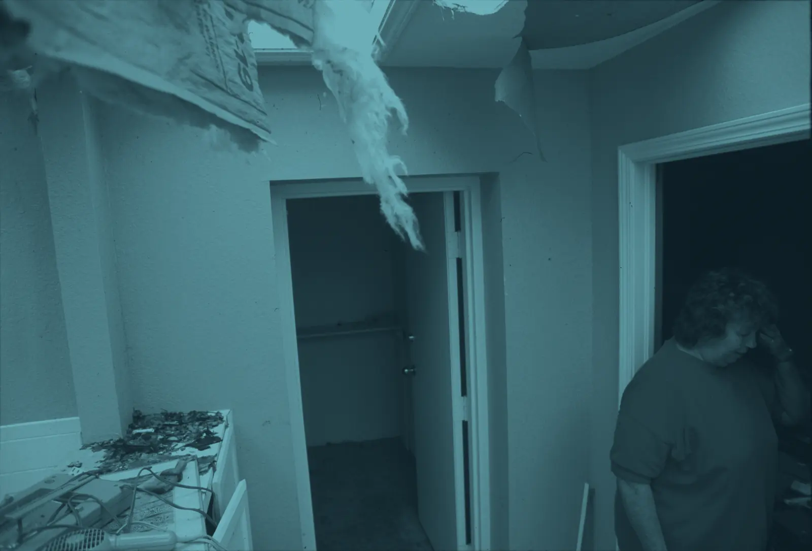A homeowner in a kitchen with the ceiling torn open after a storm
