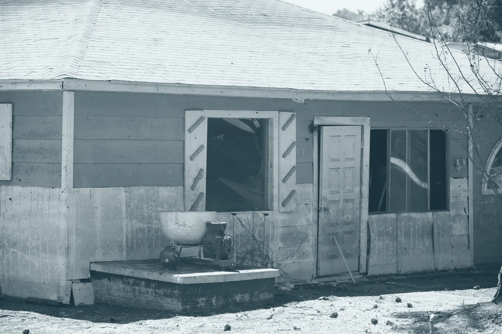 A single-storey house with blue siding above a level flood line and mud-stained siding below it, an open doorway and a boarded window