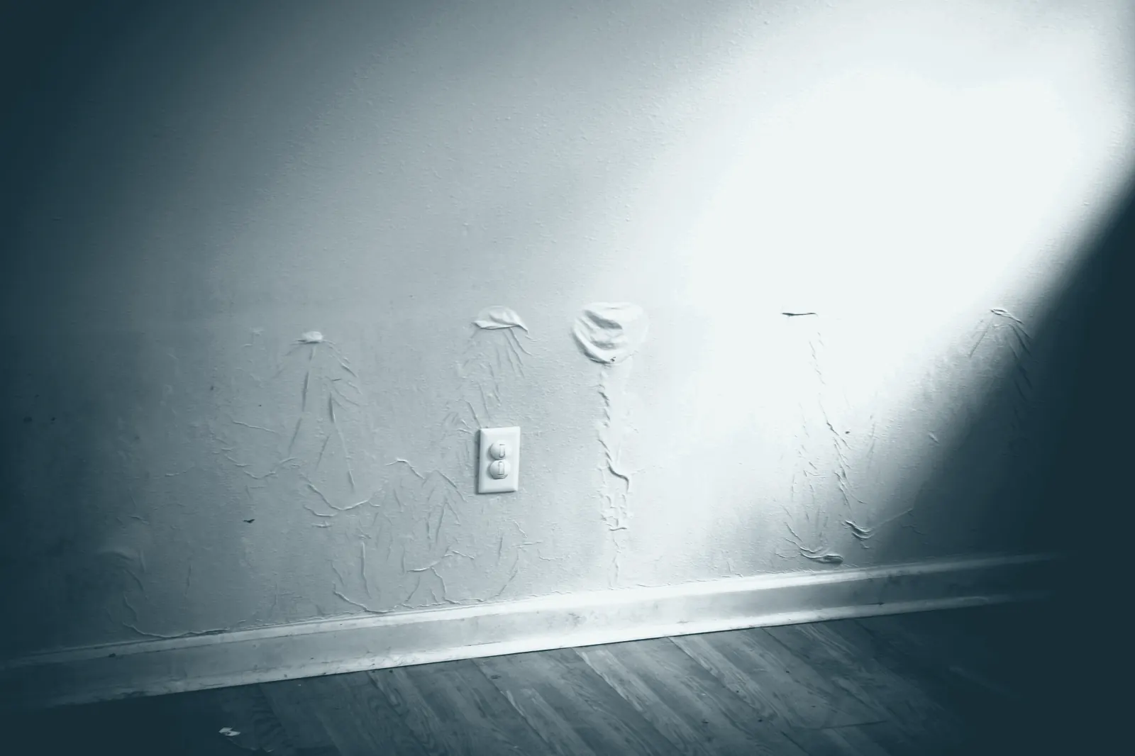 An interior wall with a flood stain across it at about waist height, blistered paint below the line, an outlet and baseboard near the floor