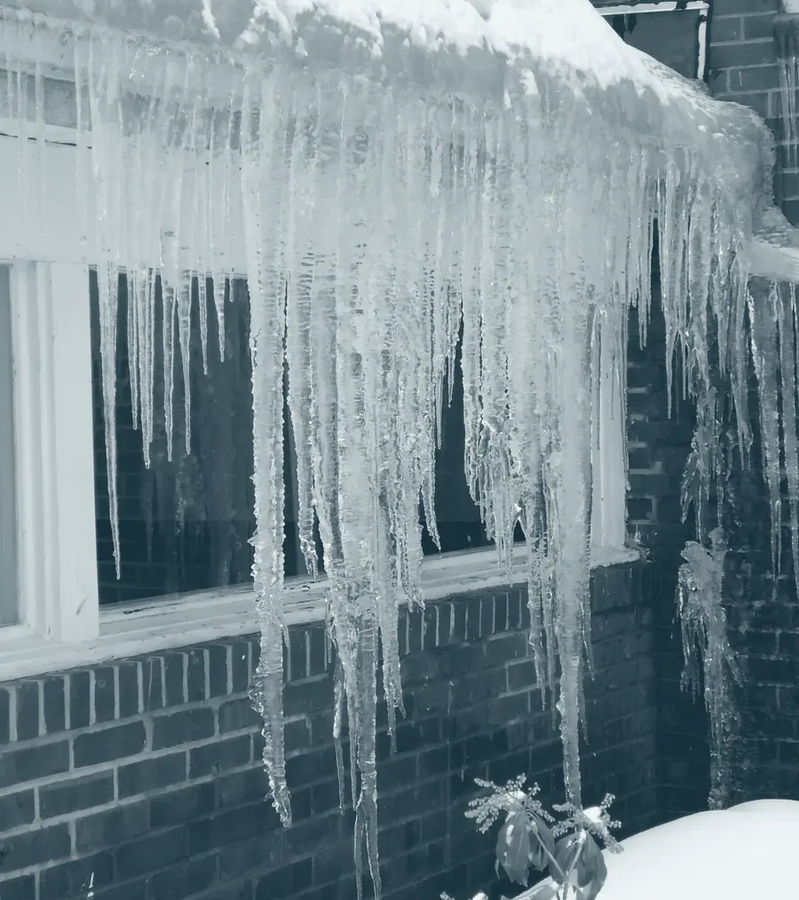 Heavy icicles hanging from the roofline of a brick building